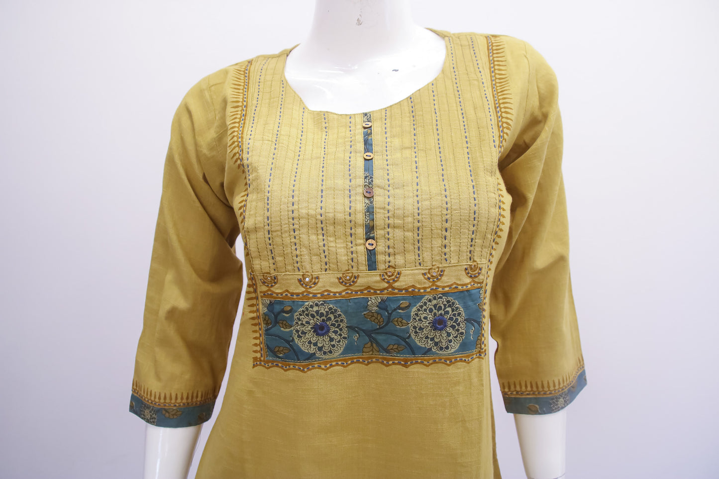 Yellow kurta with blue embroidery on a mannequin against a white background