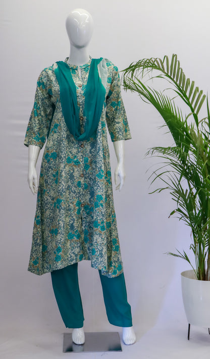 A mannequin displaying a blue dupatta set with floral print, consisting of a kurta, pant, and dupatta, standing in a retail setting with a potted plant in the background.