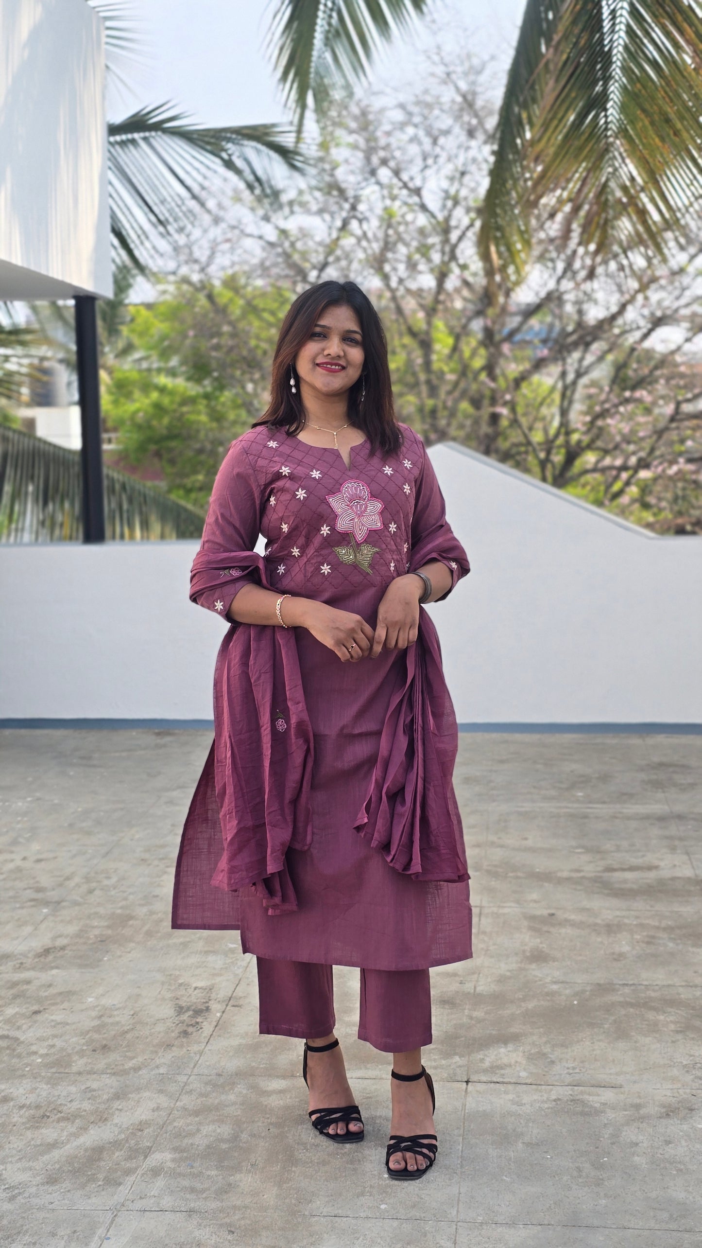 Person wearing a purple dress with floral patterns standing outdoors.