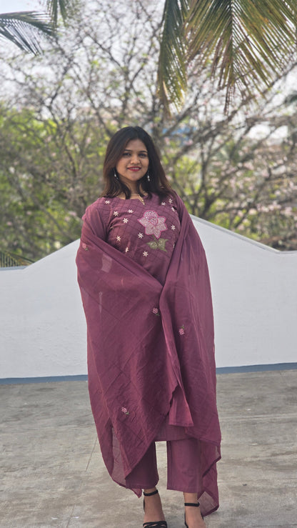 Woman wearing a maroon traditional outfit with floral patterns outdoors.
