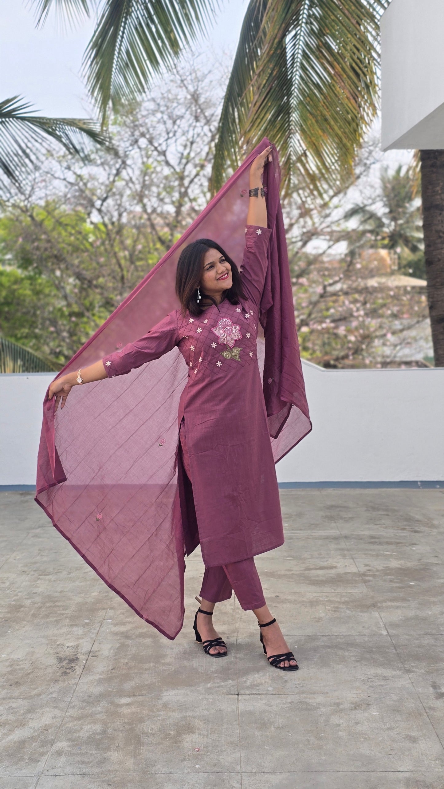 Woman in a purple outfit standing outdoors with trees in the background