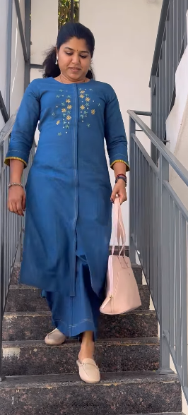 Woman in a blue outfit walking up stairs holding a pink bag.