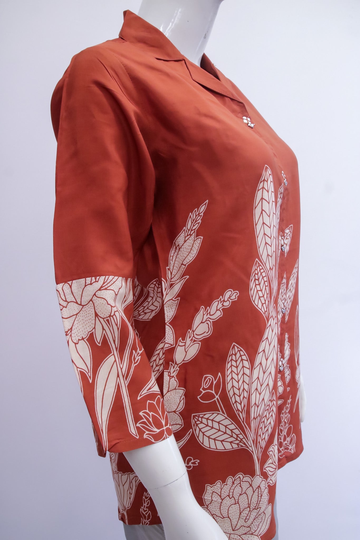 Red blouse with white floral patterns on a mannequin against a white background