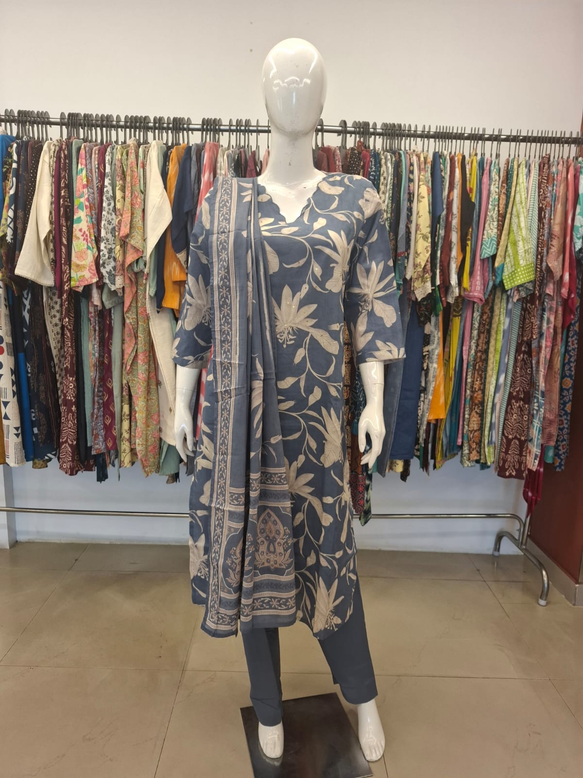 Mannequin wearing a floral dress with a rack of clothes in the background