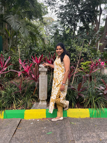 Woman in a yellow and white patterned dress standing in a garden with green and yellow curb.