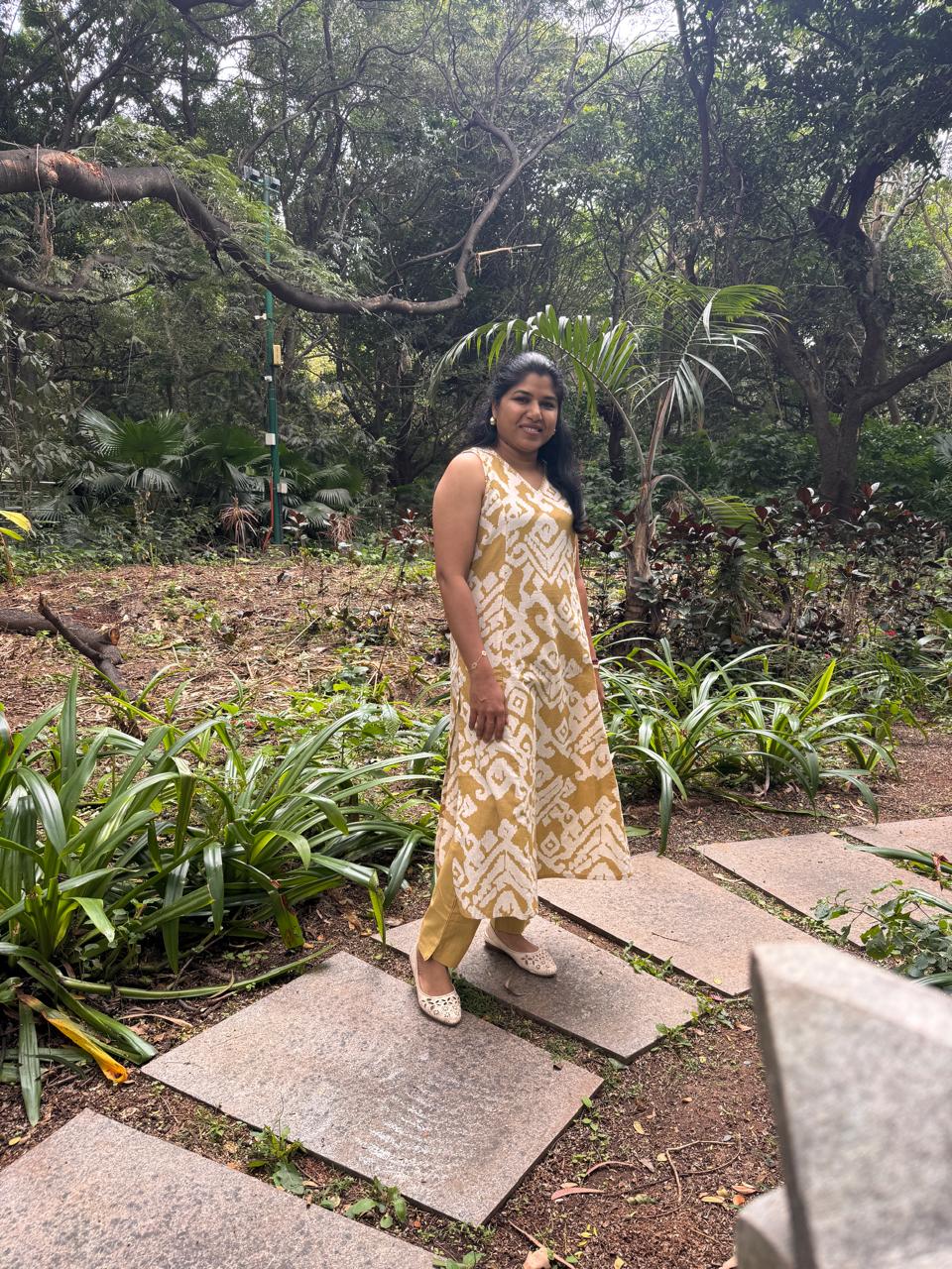 Woman in a yellow patterned dress standing on stone steps in a lush garden.