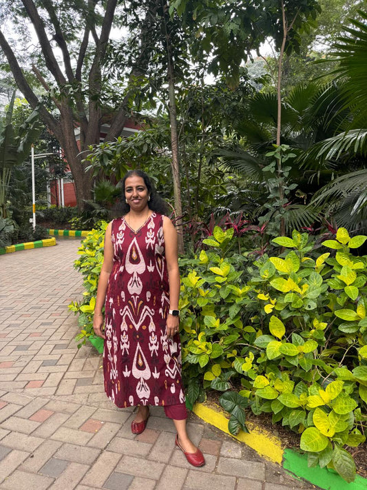 Woman in a patterned dress standing in a garden with greenery and a pathway.
