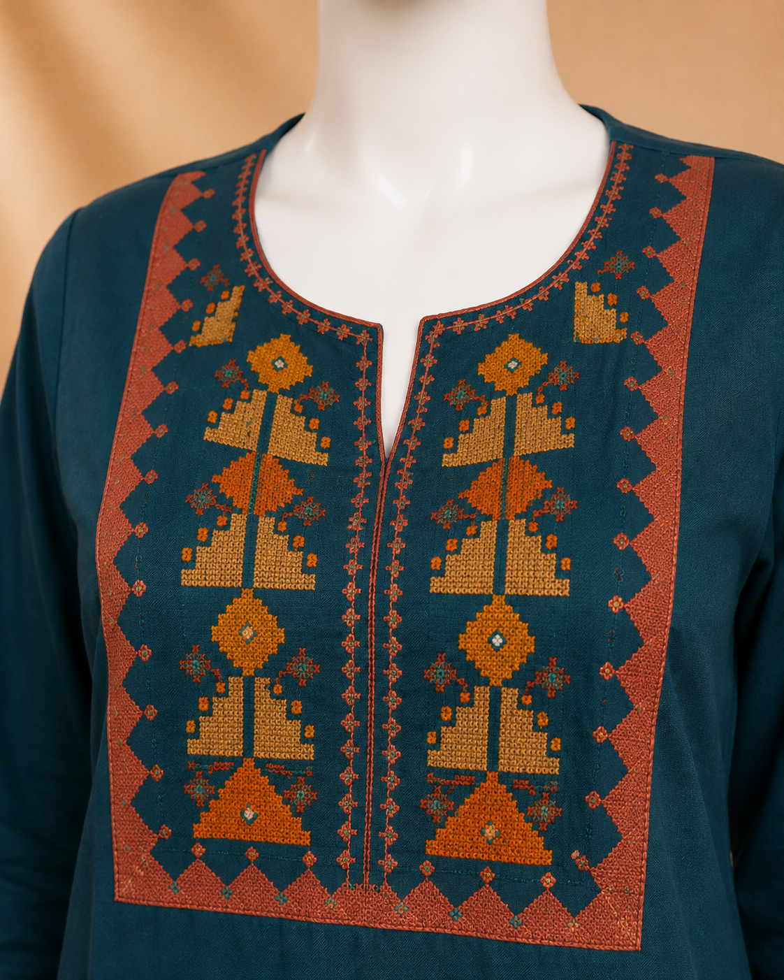 A close-up of a dark teal embroidered tunic top on a mannequin, featuring a split neckline with intricate geometric and tribal patterns in orange, brown, and gold.
