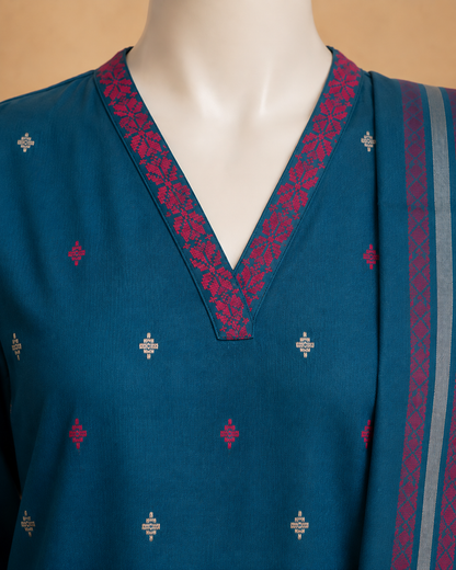 A close-up of a teal blue V-neck kurta on a mannequin, featuring magenta floral patterned trim along the neckline and scattered small metallic silver motifs on the fabric.