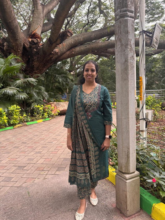 Woman in a green dress standing under a large tree with a garden background