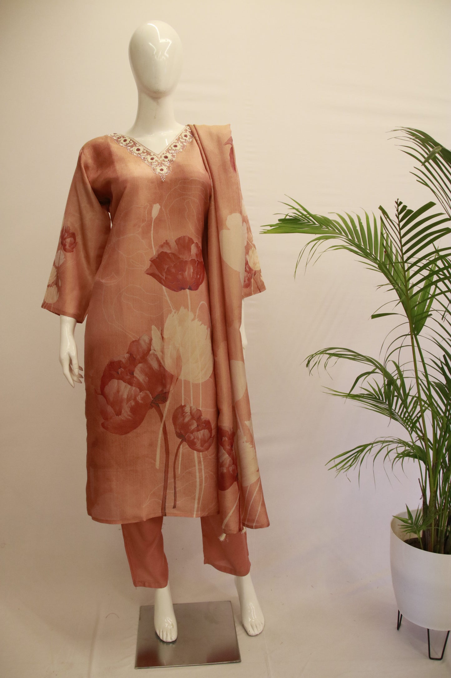 A mannequin displaying a peach-colored tissue silk dupatta set with floral print and tassels, consisting of a kurta, pants, and a dupatta.