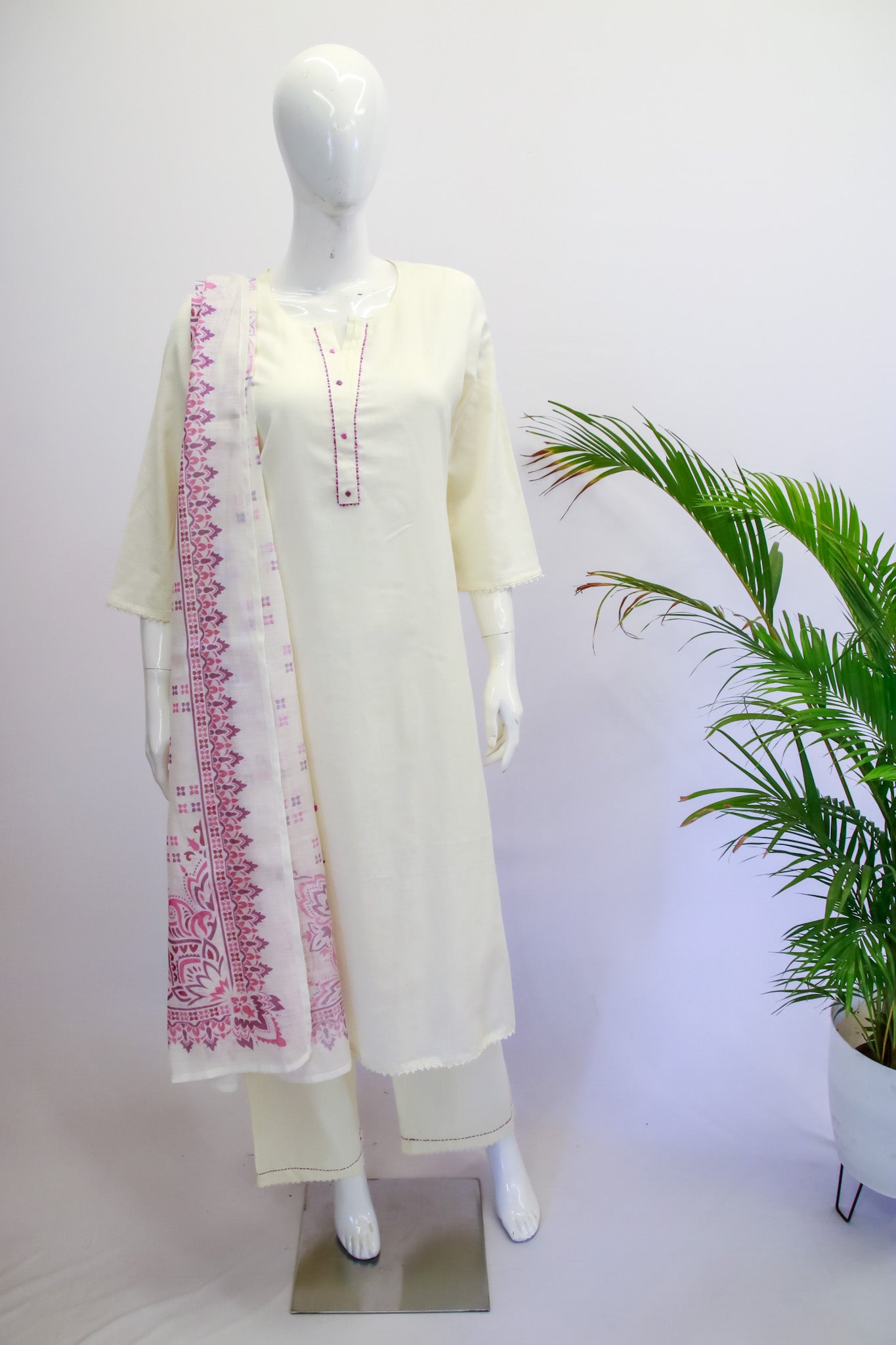 White kurta with pink embroidery on a mannequin against a white background with a plant.