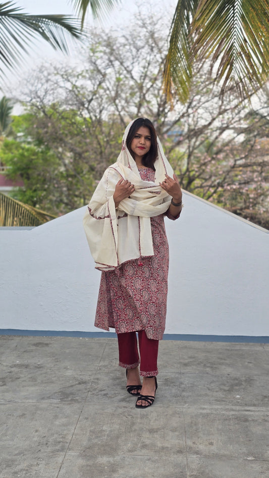 Woman in a white top and maroon skirt standing outdoors with trees in the background