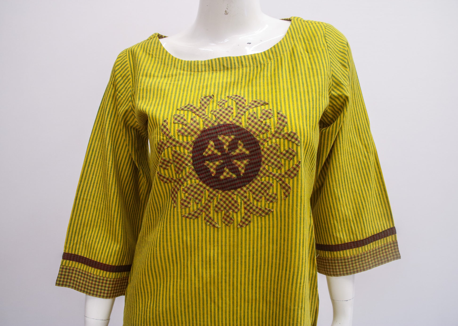 Yellow dress with brown pattern on a mannequin against a white background