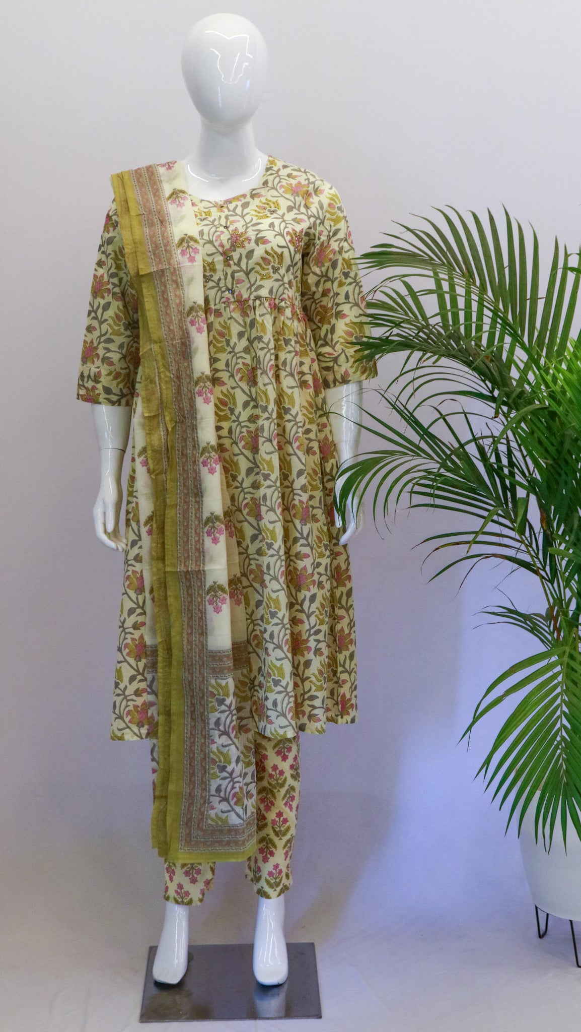 A mannequin displaying a yellow cotton dupatta set with a floral print, consisting of a kurta, pant, and dupatta, standing in a retail setting.